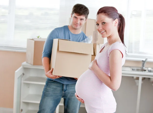 Smiling future mother in new kitchen with husband in the backgro — Stock Photo, Image