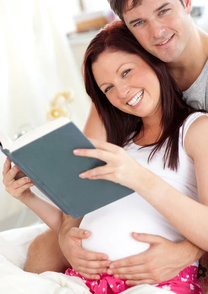 Glada framtida föräldrar läser en bok som sitter på sin säng under — Stockfoto
