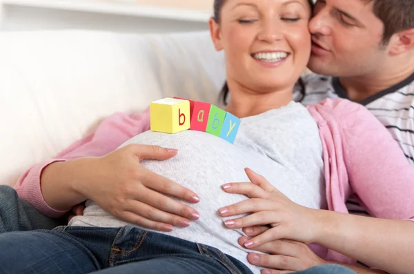 Jeune homme embrassant sa femme enceinte avec des lettres de bébé sur le bel — Photo