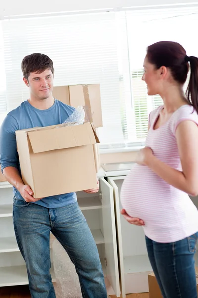 Smiling man with cardboard looking at his pregnant wife standing — Stock Photo, Image
