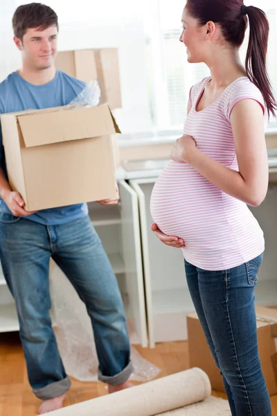 Милая беременная жена смотрит на своего мужа, держащего коробку стоя. — стоковое фото