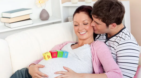 Young man kissing his pregnant wife with baby letters on the bel — Stock Photo, Image