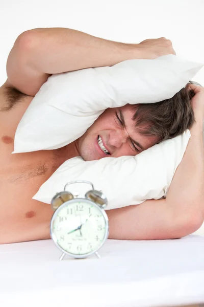 Hombre enojado despertado por su despertador poniendo almohada en su cabeza — Foto de Stock