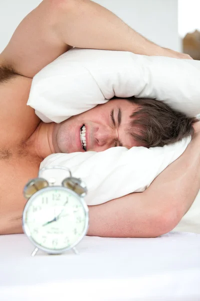 Stressed man woken-up by his alarm clock putting his head under — Stock Photo, Image