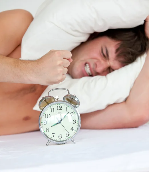 Angry man stressed by his alarm clock lying on his bed — Stock Photo, Image
