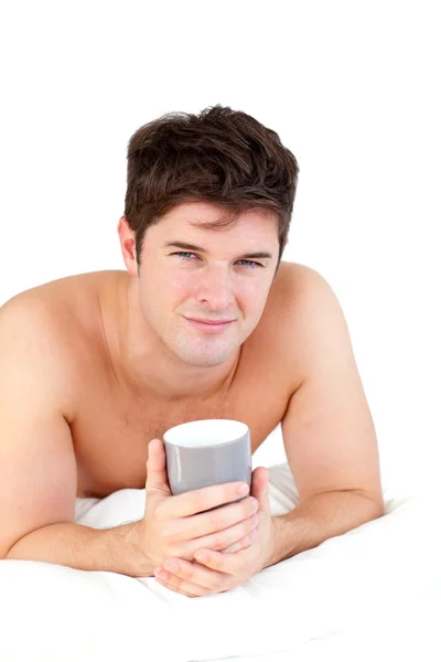Young male adult holding a cup of tea lying on his bed — Stock Photo, Image