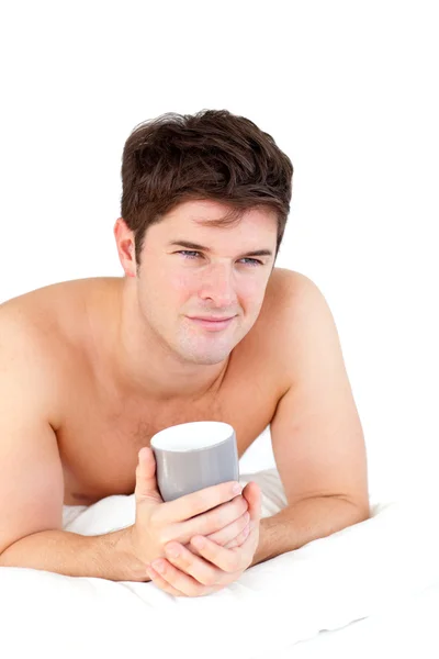 Young male adult in pyjamas holding a cup of tea lying on his be — Stock Photo, Image