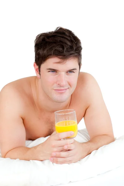 Bonito hombre acostado en su cama con un vaso de jugo de naranja — Foto de Stock