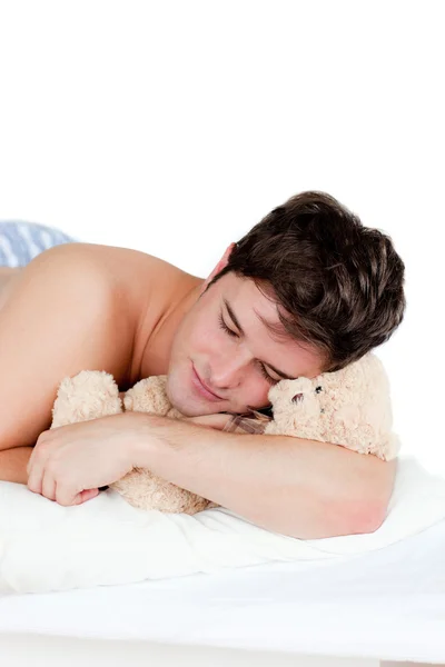 Молодой человек в пижаме спит с плюшевым мишкой, лежащим на его кровати — стоковое фото
