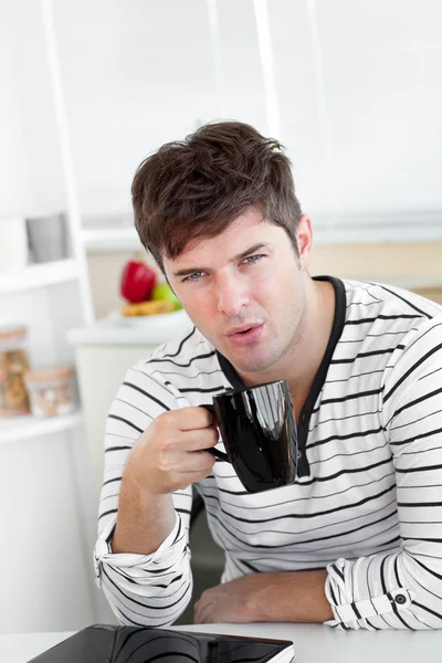 Yakışıklı adam mutfakta oturmuş kahve fincanını üfleme — Stok fotoğraf