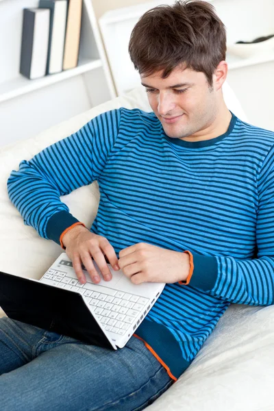 快乐的年轻人使用他躺在沙发上的笔记本电脑 — 图库照片