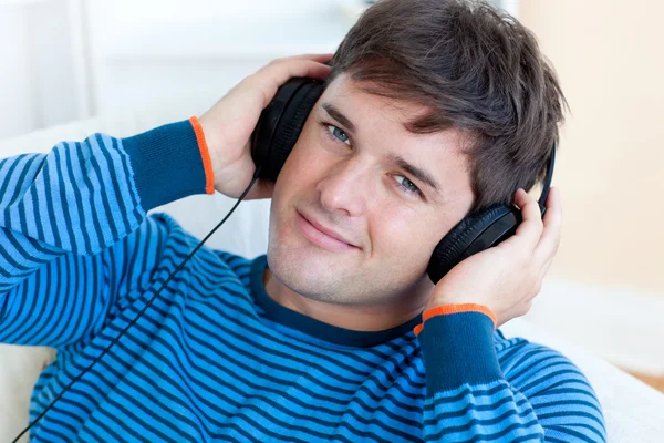 Cheerful man listening music with headphones on lying in the liv — Stock Photo, Image