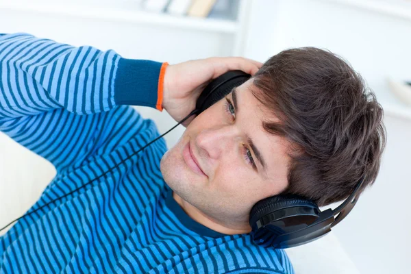 Šťastný mladý muž se sluchátky relaxační hudbou na pohovce — Stock fotografie