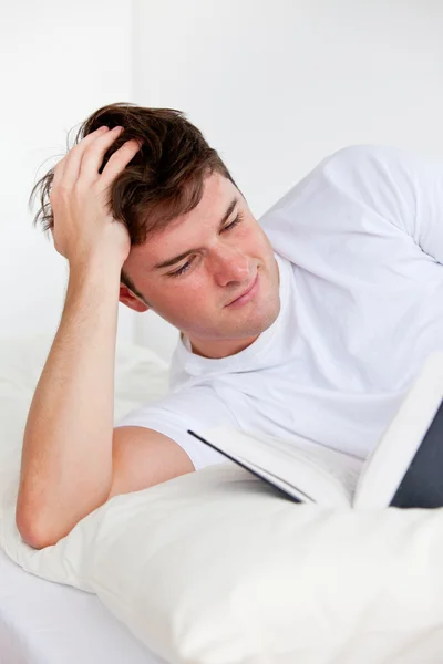 Молодой человек читает книгу, лежащую на его кровати — стоковое фото