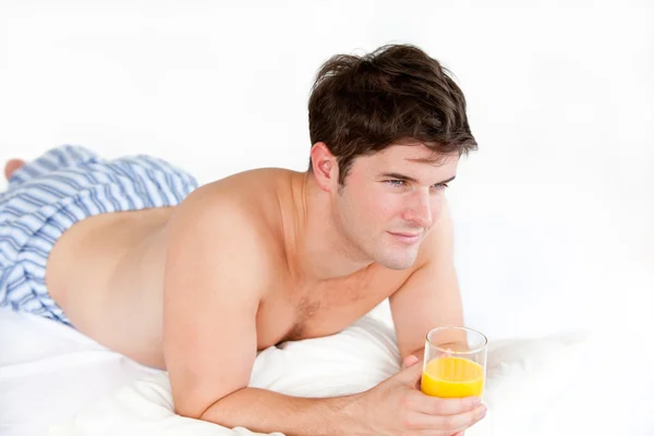 Handsome boy in pyjamas holding a glass of orange juice lying on — Stock Photo, Image