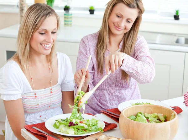 Två glada kvinnor äter sallad i köket — Stockfoto