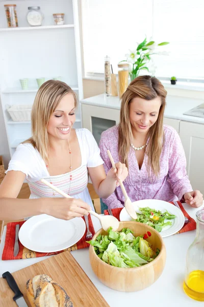 Two glowing female friends eating salad in the kitchen — Stock Photo, Image