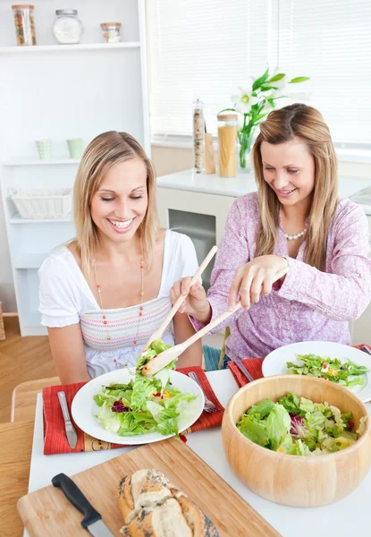 Två glada väninnor äta sallad i köket — Stockfoto