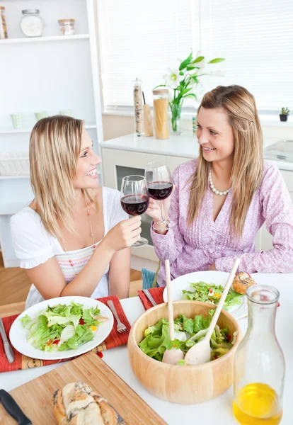 Duas amigas alegres comendo salada na cozinha — Fotografia de Stock