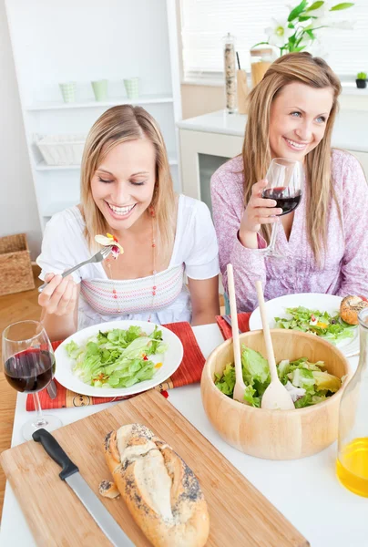 Duas amigas encantadas comendo salada na cozinha — Fotografia de Stock