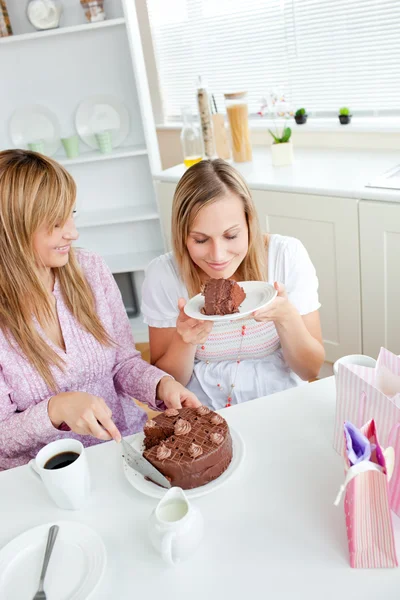 Delighted female friends eating a chocolate cake in the kitchen — Stock Photo, Image