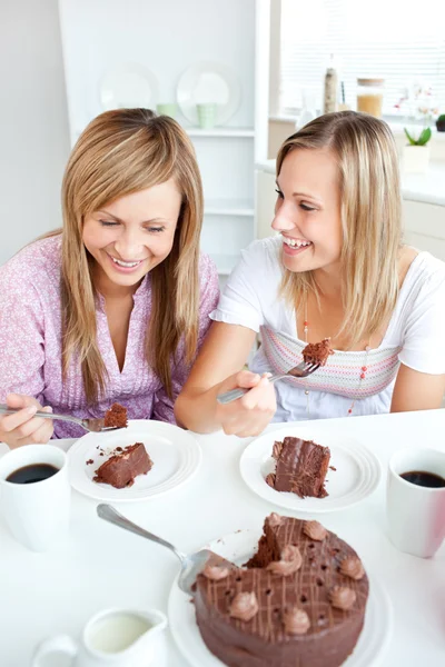 Fröhliche Freundinnen essen einen Schokoladenkuchen in der Küche — Stockfoto
