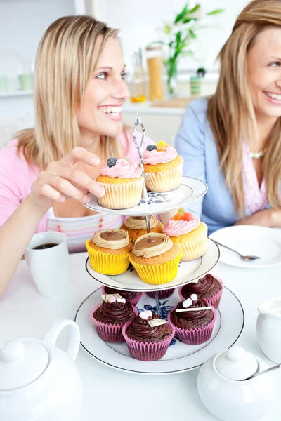 Portrait of two smiling female friends eating pastries in the ki — Stock Photo, Image