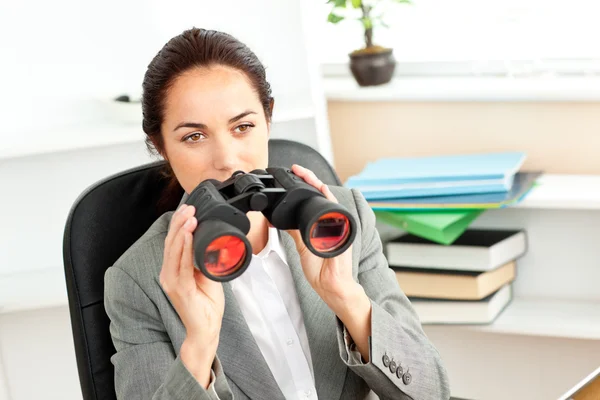 Serious hispanic businesswoman looking through binoculars sittin — Stock Photo, Image