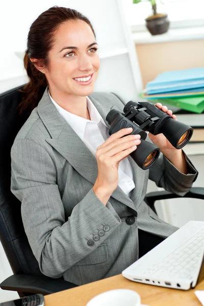 Radiant hispanic businesswoman holding binoculars sitting at her — Stock Photo, Image
