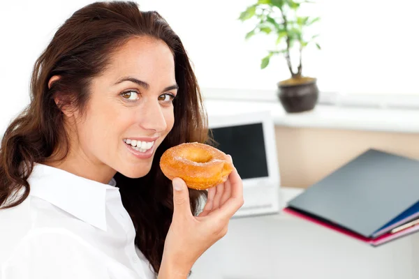 Happy hispanic businesswoman eating a doughnut — Stok fotoğraf
