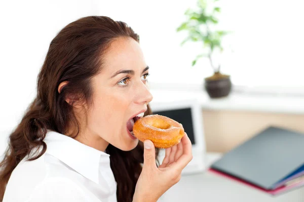 Cute hispanic businesswoman eating a doughnut — Stok fotoğraf