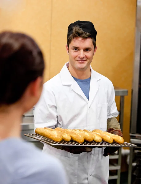 Сяючий молодий чоловік пекар тримає багети на кухні — стокове фото