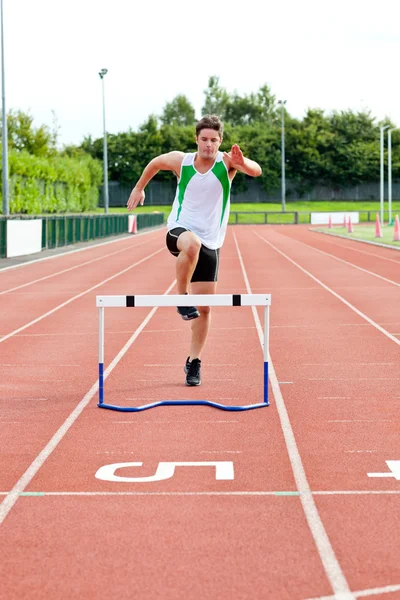 Hombre deportivo saltando por encima del seto durante una carrera —  Fotos de Stock
