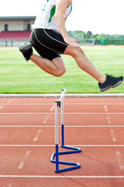 Bestemt mannlig idrettsutøver som hopper over hekken under et løp – stockfoto