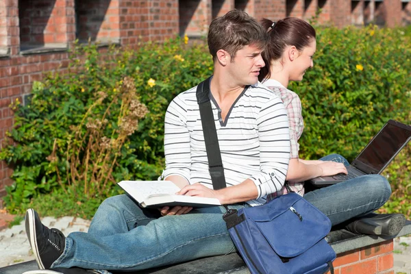 Serious couple of students working together with book and laptop — Stock Photo, Image