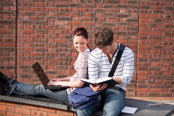 Two students working together with book and laptop outside — Stock Photo, Image