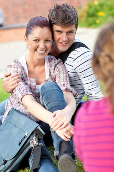 Jovem casal de estudantes sentados na grama conversando com uma fêmea — Fotografia de Stock