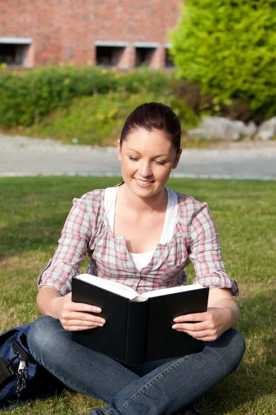 Χαλαρή φοιτήτριας, διαβάζοντας ένα βιβλίο που κάθεται στο γρασίδι — Φωτογραφία Αρχείου