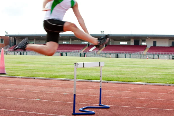 Seriøs mannlig atlet som hopper over hekken under et løp – stockfoto