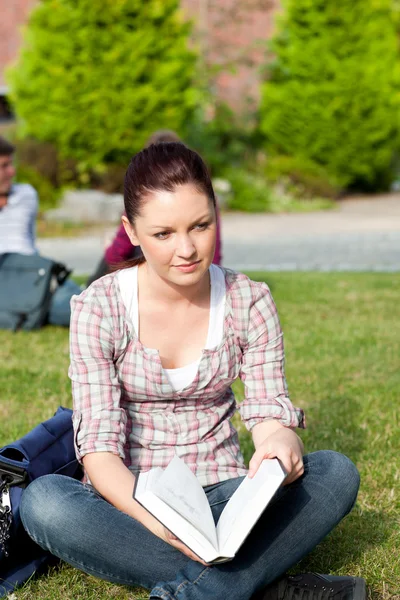 Estudiante pensativa leyendo un libro sentado en la hierba — Foto de Stock