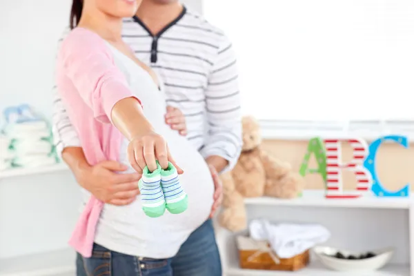 Close-up of a bright pregnant woman holding baby shoes while hus — Stock Photo, Image