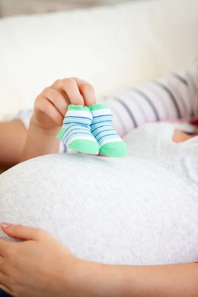Close-up van de buik van een zwangere vrouw met baby schoenen — Stockfoto