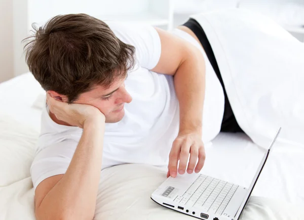 Sevimli adam yatağında yatan bir dizüstü bilgisayar kullanarak — Stok fotoğraf