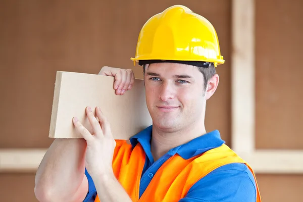 Jovem trabalhador masculino carregando uma tábua de madeira — Fotografia de Stock