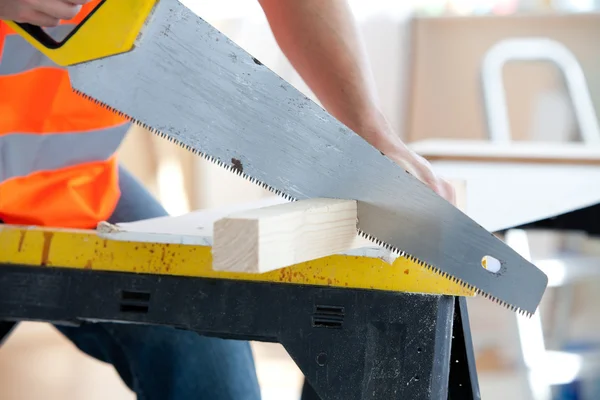 Close-up de um trabalhador masculino sério serrar uma tábua de madeira — Fotografia de Stock
