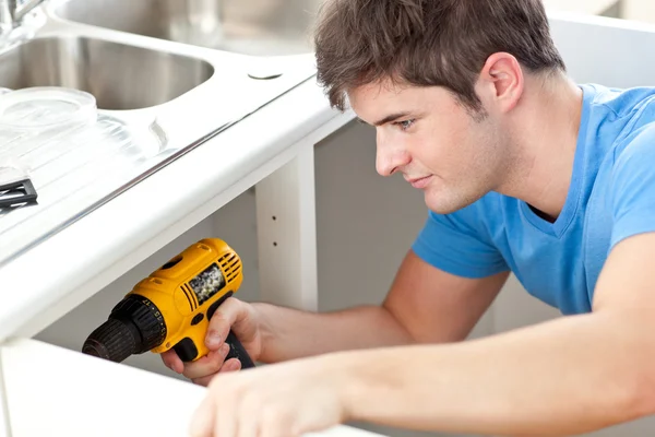 Uomo sicuro di sé con un trapano che ripara un lavandino della cucina — Foto Stock