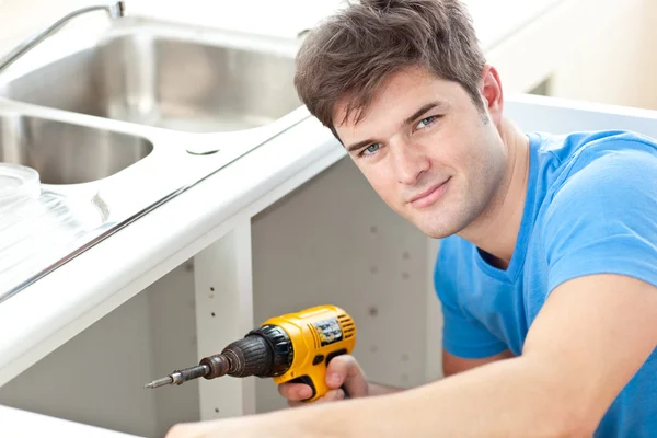 Handsome man holding a drill repairing a kitchen sink — Stock Photo, Image
