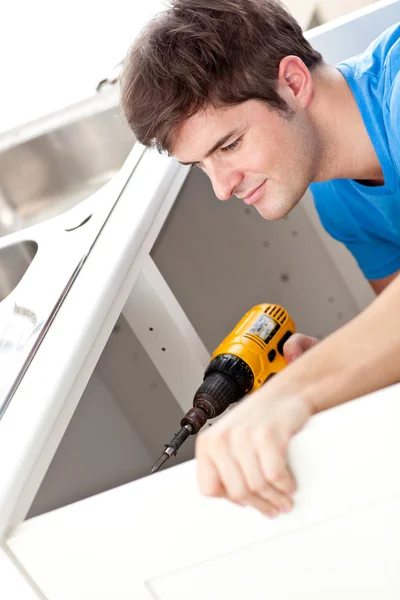 Un uomo sicuro che tiene un trapano per riparare un lavello della cucina — Foto Stock