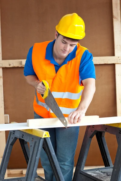Bonito trabalhador masculino vestindo um chapéu amarelo serrar um bo de madeira — Fotografia de Stock