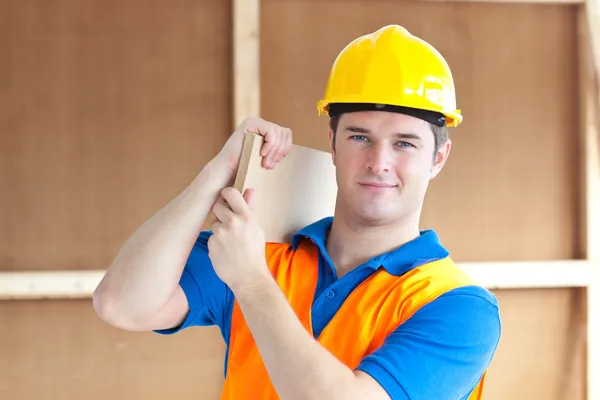 Joven trabajador confiado con un casco amarillo que lleva una madera —  Fotos de Stock